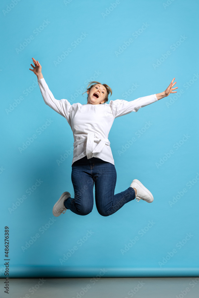 Full-length portrait of excited young girl jumping isolated on blue background. Concept of wow emotions, facial expressions, ad, sales