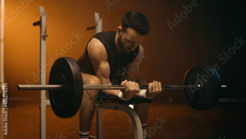 Athletic sportsman working out with barbell on dark background