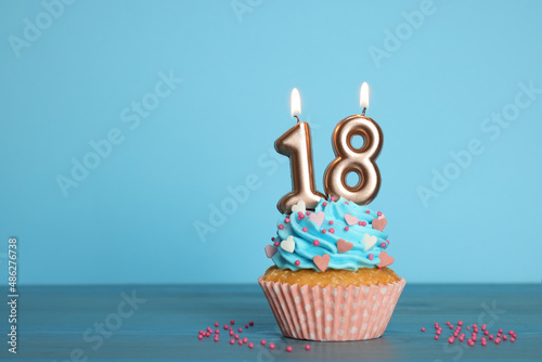 Coming of age party - 18th birthday. Delicious cupcake with number shaped candles on light blue background, space for text photo