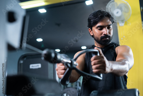 young man busy exercising for chest while listening music on wireless headphone at gym - concept of body building, morning routine and fit healthy lifestyle.