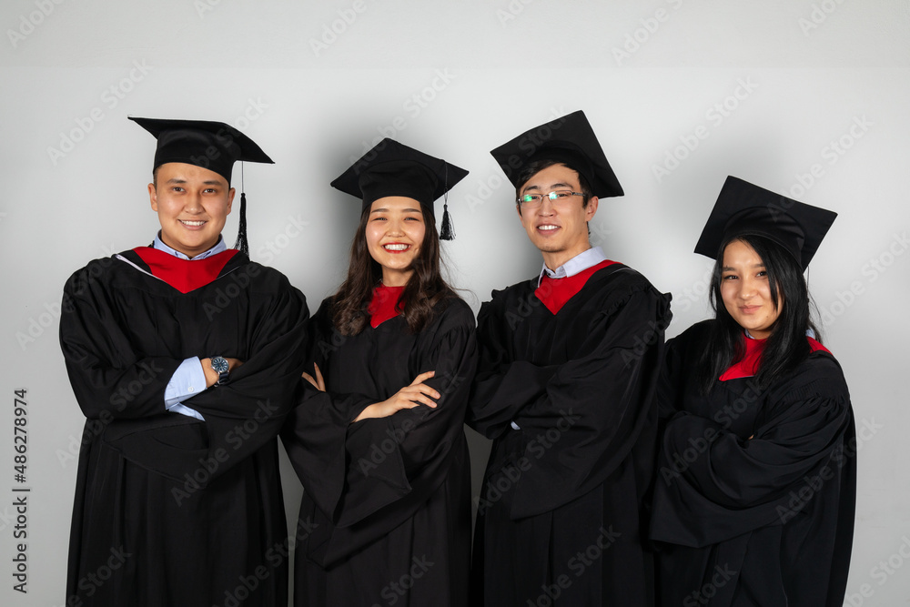 Group of graduate students friends pose together smiling in gowns and capes
