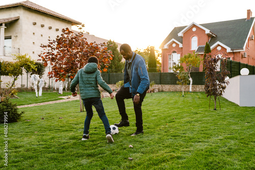 Black man playing football with his son on backyard