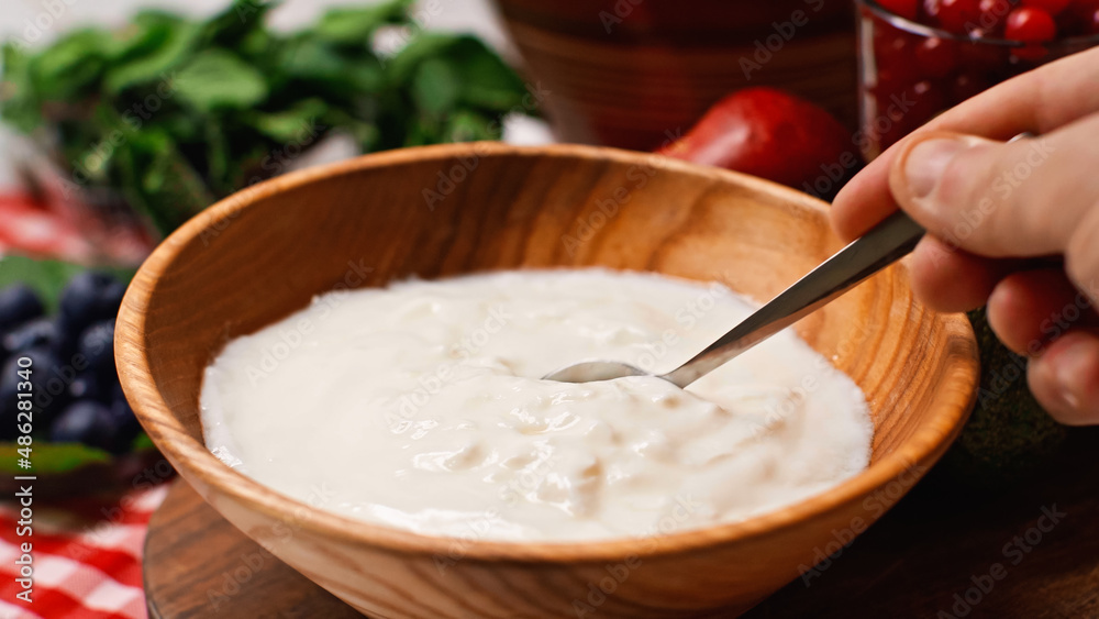 partial view of man holding spoon near yogurt in bowl partial view of man holding spoon near yogurt in bowl