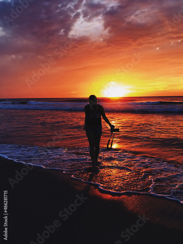 Dark silhouette of a woman with a camera on the ocean in an burning orange sunset © asauriet
