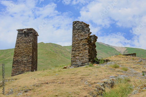 Ushguli fortified village in Svanetia, Georgia. Grey, brown and biege medieval stone towers left from queen's Tamara castle. Yellow dry grass and blue sky with clouds