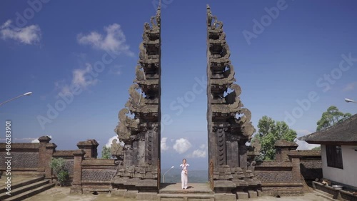 Woman in white dress praying, standing in Famous Bali gates, historical sacred sightseeing in Indonesia
