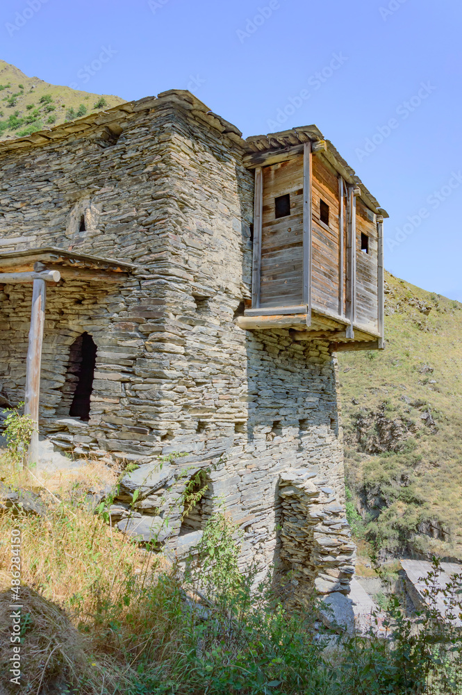 Abandoned grey stone living tower in Shatili medieval fortified village in Khevsuretia, Georgia. Blue sky and green mountain slopes