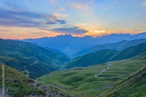 View of the summer sunset above the caucasian mountains from the Bear Cross mountain pass in Khevsureti, Georgia. Blue and orange sky with clouds, green and blue haze maountains, road to Shatili photo