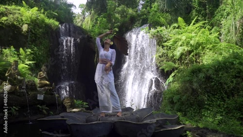 Feminity and nature concept, astonishing woman dancing in front of a huge majestic tropical waterfall