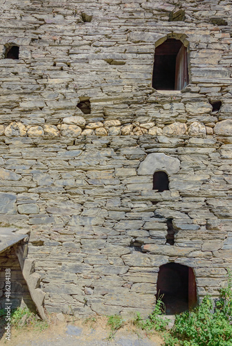 Abandoned grey stone living tower in Shatili medieval fortified village in Khevsuretia, Georgia. Old grey stone wall with dark windows and arch doorway. Cut-off human hands are carved above the window photo