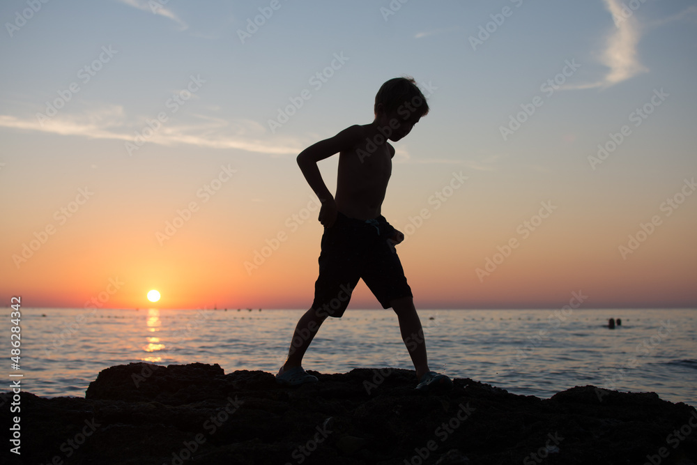 Fototapeta premium Silhouette of a person on the beach at sunset. Kid and vacation concept.