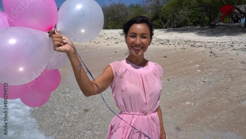 Romantic birthday surprise on the ocean coast, cheerful woman in pink dress holding balloons, true happiness