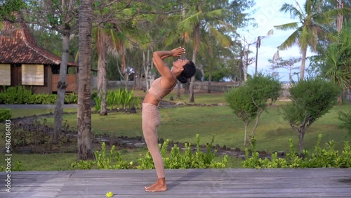 Yoga teacher lady doing Sun Salutation practise outdoors on the exotic island nature with palm trees 