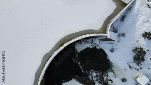 Top Down Drone Aerial View of Dam and Frozen Snow Capped Lake on Cold Winter Day photo