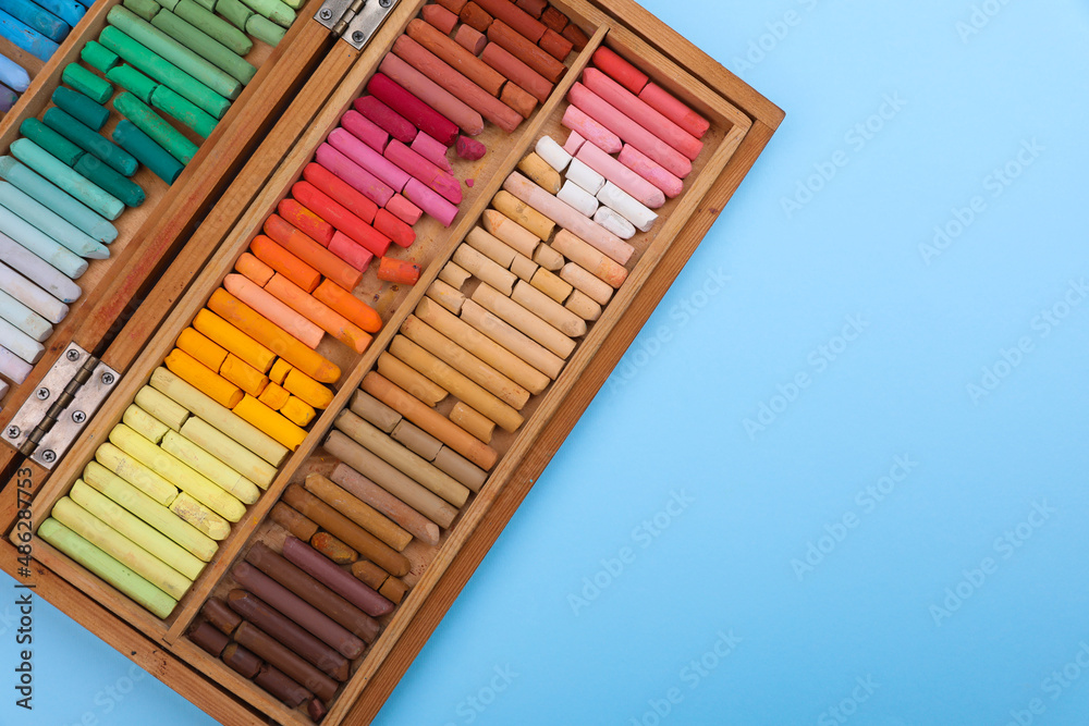 Obraz premium Set of soft pastels in wooden box on light blue background, top view with space for text. Drawing material