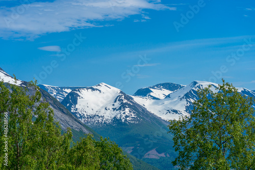 Spring time in Norway with mountains with snow and green trees.