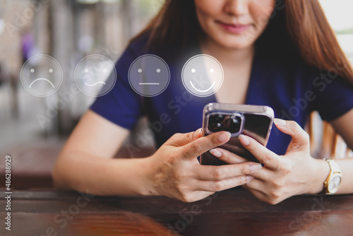 Customer Experience Concept, happy Business women holding the smartphone with visual screen of Excellent Smiley Face and Rating for a satisfaction survey.
