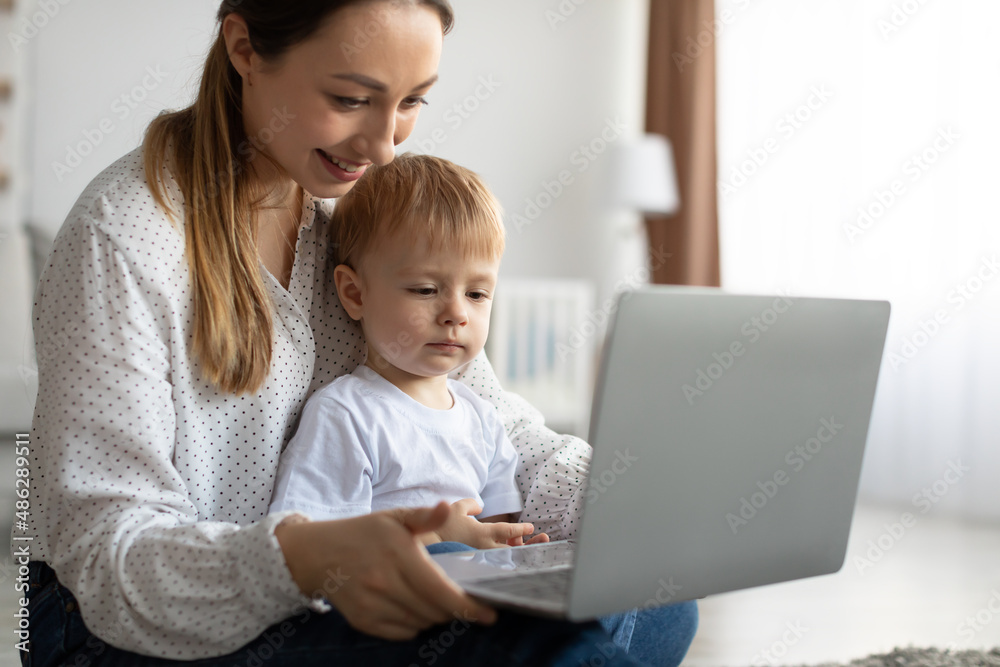 Happy single mother and little son using laptop online application, making video call or watching cartoons together Happy single mother and little son using laptop online application, making video call or watching cartoons together