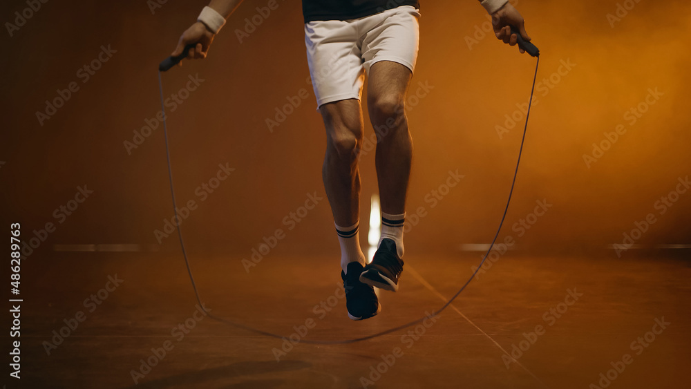 Cropped view of athletic sportsman jumping with rope on dark background - obrazy, fototapety, plakaty 