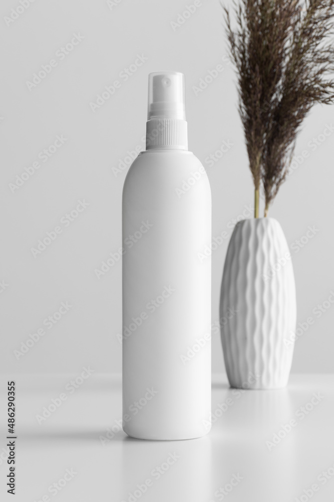 White cosmetic spray bottle mockup with a dry flower on the white table.  Photos | Adobe Stock