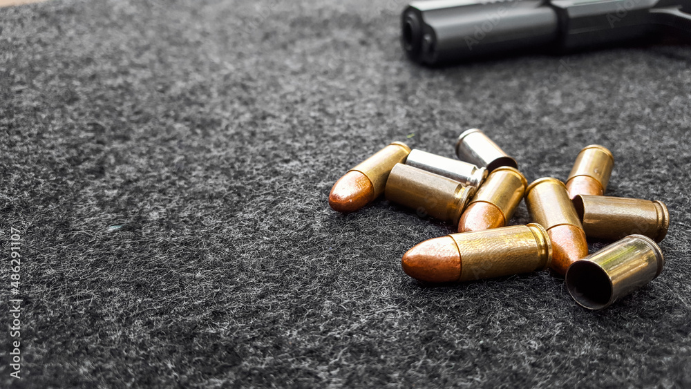 Black artificial handgun and bullets on dark gray fabric. Concept for security of social, personal and shooting sport equipments