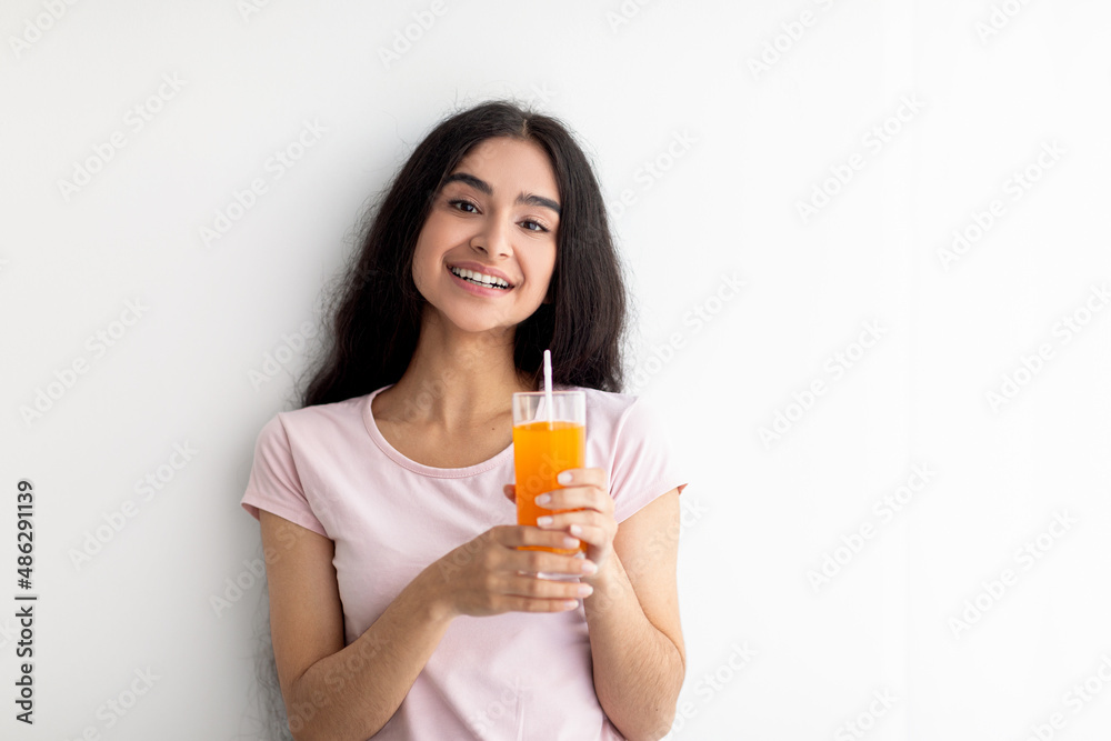 Cheerful young Indian woman holding glass of fresh orange or mango juice on white background, copy space Cheerful young Indian woman holding glass of fresh orange or mango juice on white background, copy space