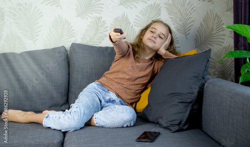 selective focus on little girl sitting on sofa and holding remote control in hand while watching cartoon, tv show and video for kids