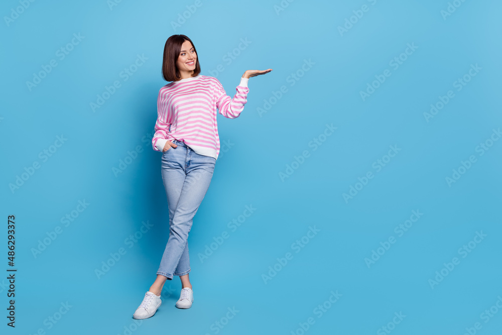 Photo of charming pretty woman wear striped sweater holding arm empty space isolated blue color background Photo of charming pretty woman wear striped sweater holding arm empty space isolated blue color background