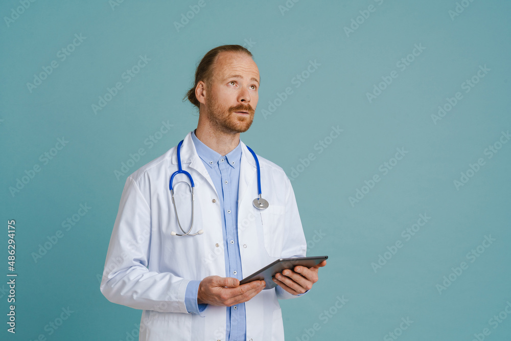 White male doctor wearing lab coat using tablet computer White male doctor wearing lab coat using tablet computer