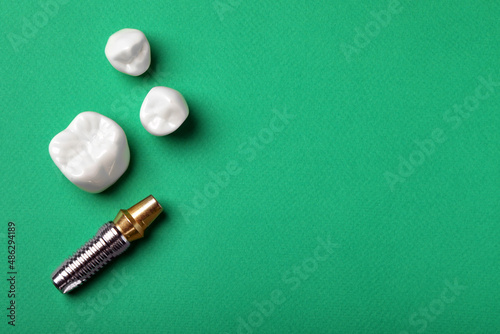 Post and abutment of dental implant near different crowns on green background, flat lay. Space for text photo