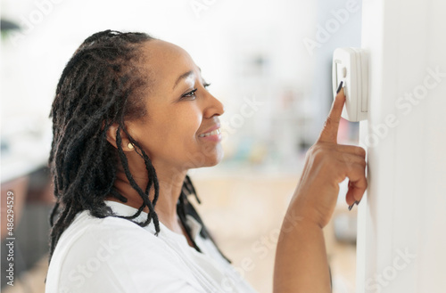 A frican woman lady adjusting the climate control panel on the wall wall thermostat