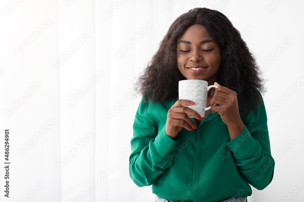 Relaxed black woman standing by window, drinking coffee Relaxed black woman standing by window, drinking coffee