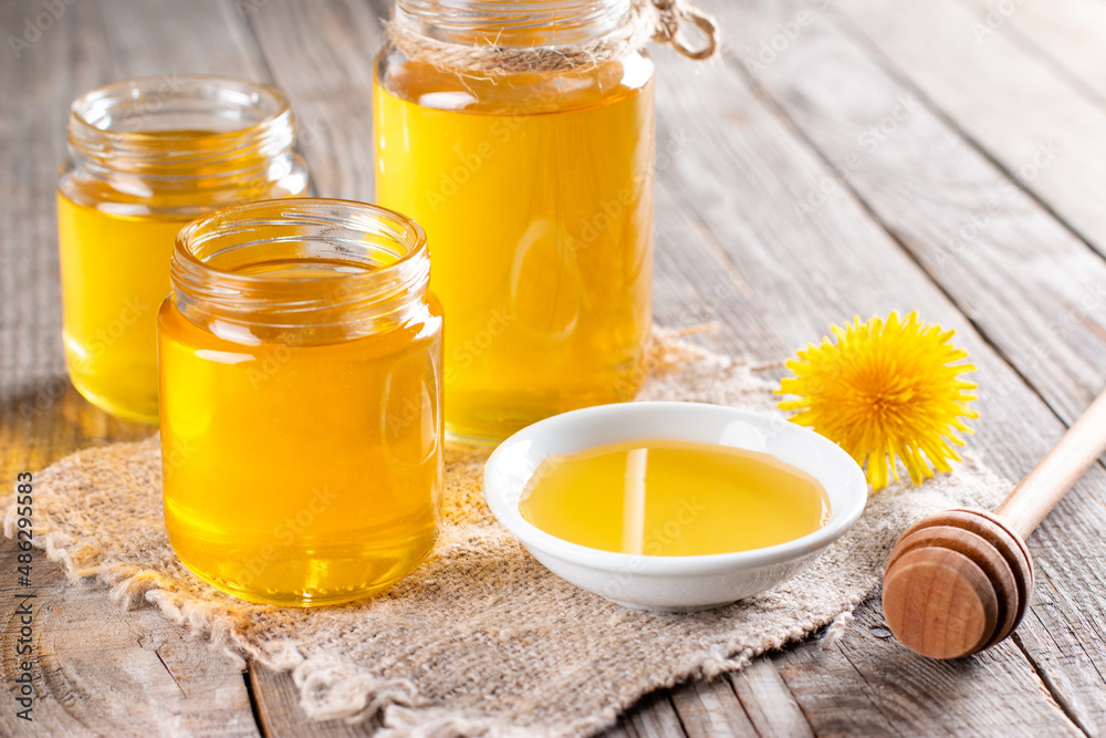 Flower honey in a glass jar and dandelions on a table Flower honey in a glass jar and dandelions on a table