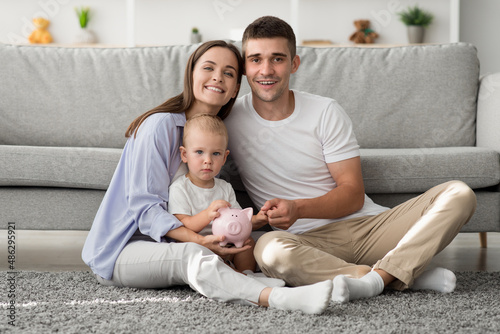 Family Economy. Happy Mother  Father And Toddler Child Holding Piggy Bank