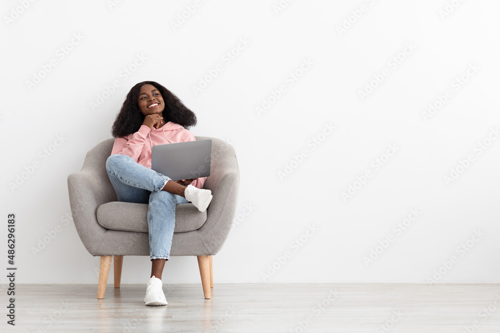Pretty black lady sitting in armchair with laptop, copy space