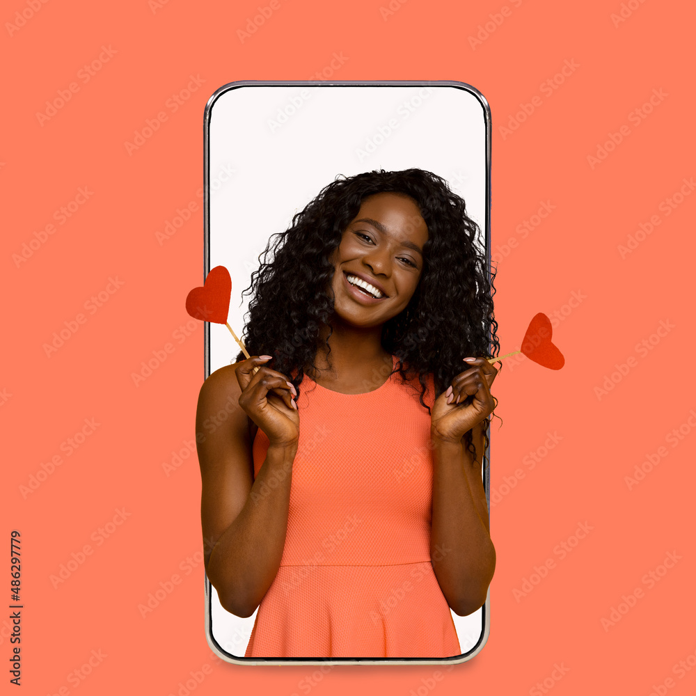Happy cheerful young pretty african american woman hold hearts on empty screen of big phone isolated