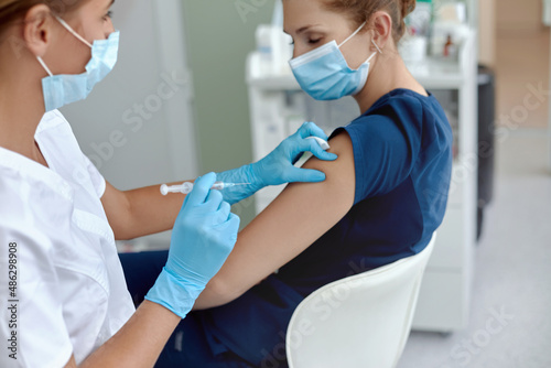 woman doctor or nurse giving shot or vaccine to patient shoulder.