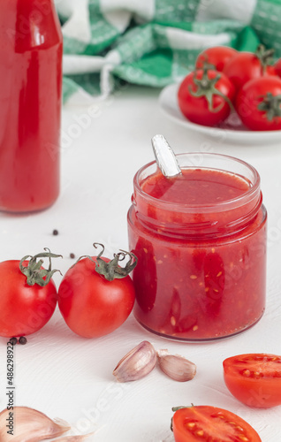 Fresh tomato sauce in a glass bottle, red cherry tomatoes and a garlic on a white background. Healthy eating concept.