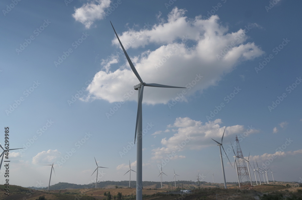 Evening atmosphere of Windmills farm field with white clouds scattered against the blue sky. The electricity energy generating wind turbine. The concept of using the use of renewable wind to generate Evening atmosphere of Windmills farm field with white clouds scattered against the blue sky. The electricity energy generating wind turbine. The concept of using the use of renewable wind to generate