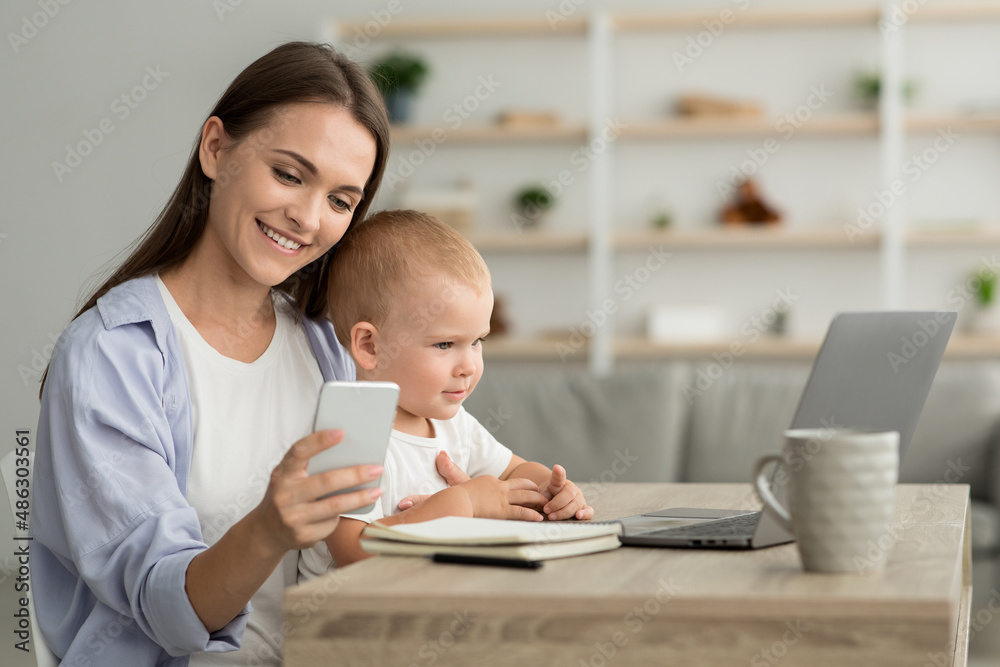 Remote Career. Young Mom With Baby On Hands Using Smartphone And Laptop Remote Career. Young Mom With Baby On Hands Using Smartphone And Laptop