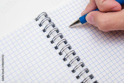 Writing notes or planning a schedule on blank spiral notebook, hand using a pen on a checkered blank paper, copy space