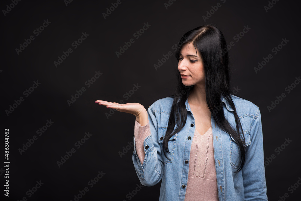 Attractive caucasian brunette girl in shirt looking at palm with copy space for advertising isolated on black studio background. Attractive caucasian brunette girl in shirt looking at palm with copy space for advertising isolated on black studio background.