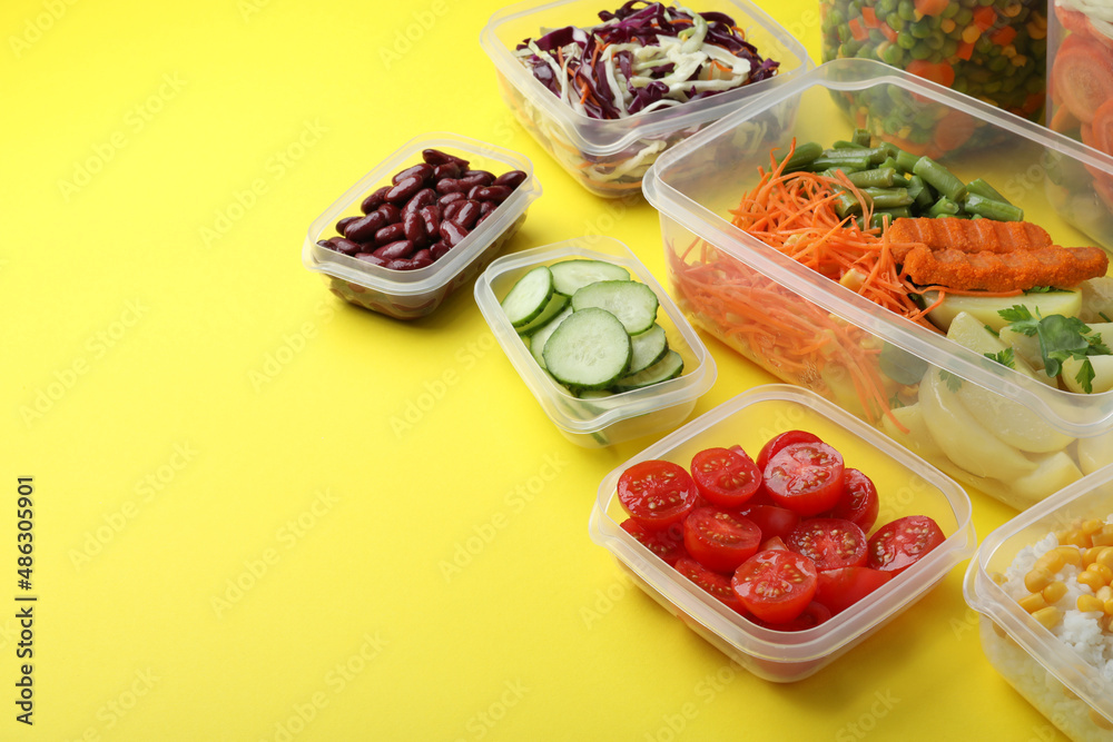 Set of plastic containers with fresh food on yellow background, space for text