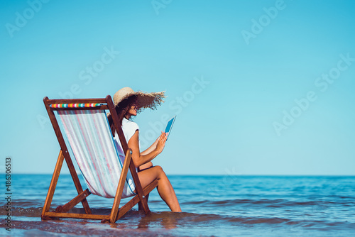 Photo Back view of woman in sunhat who using laptop while lying on the beach chaise lo