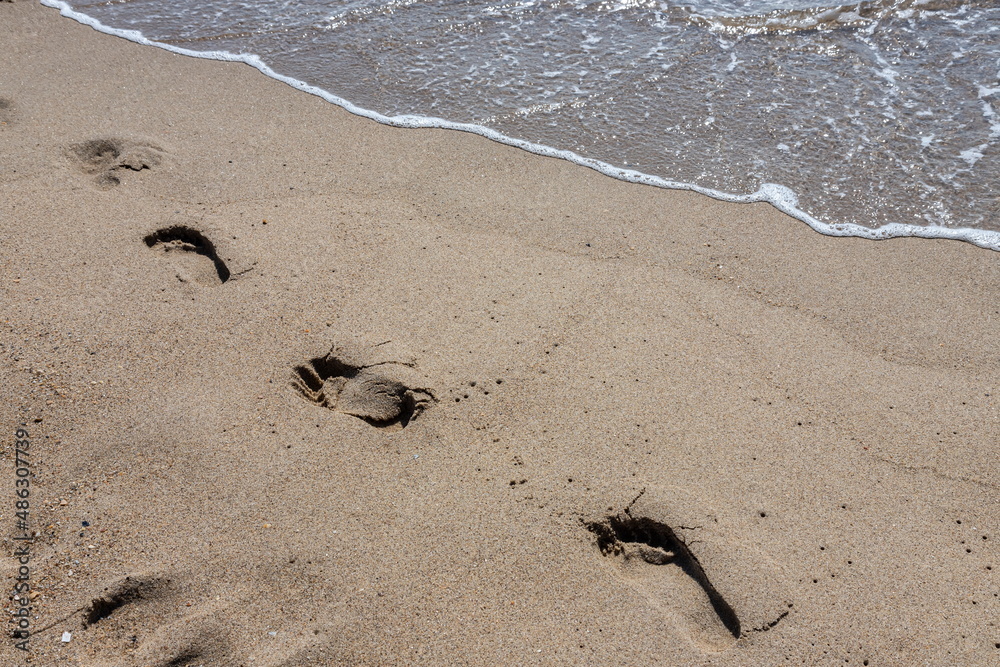 Obraz premium Footprints of a man on the yellow beach sand from walking barefoot by the sea with water that washes away the footprints.