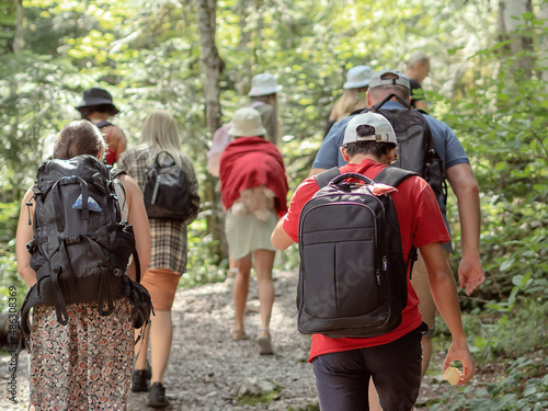 A group of people with backpacks go into the thicket of a deciduous forest on a summer sunny day. Hiking in the national reserve. Back view. Sost focus © jockermax3d