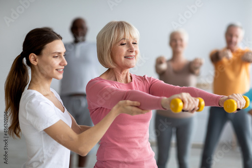 Tableau sur toile Young lady coach helping senior woman while exercising
