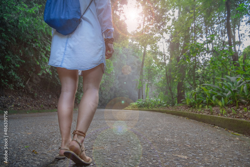 A girl with a rag backpack and dirty feet walks along the road through the jungle view from her feet close-up in sun glare