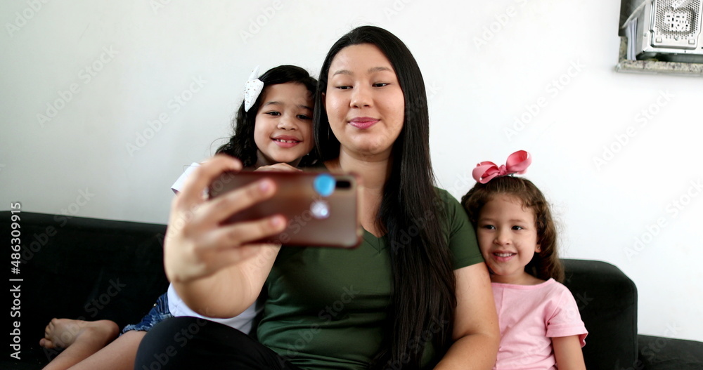Obraz premium Asian mother taking selfie with two little daughters at home, holding smartphone