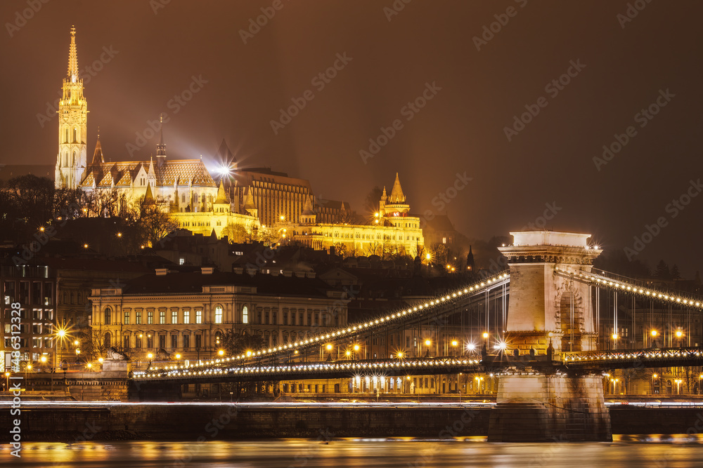 Budapest, Hungary night view of Chain Bridge Szechenyi Lanchid on Danube river. Illuminated landscape of Castle District with Fisherman Bastion and Matthias Church visible.